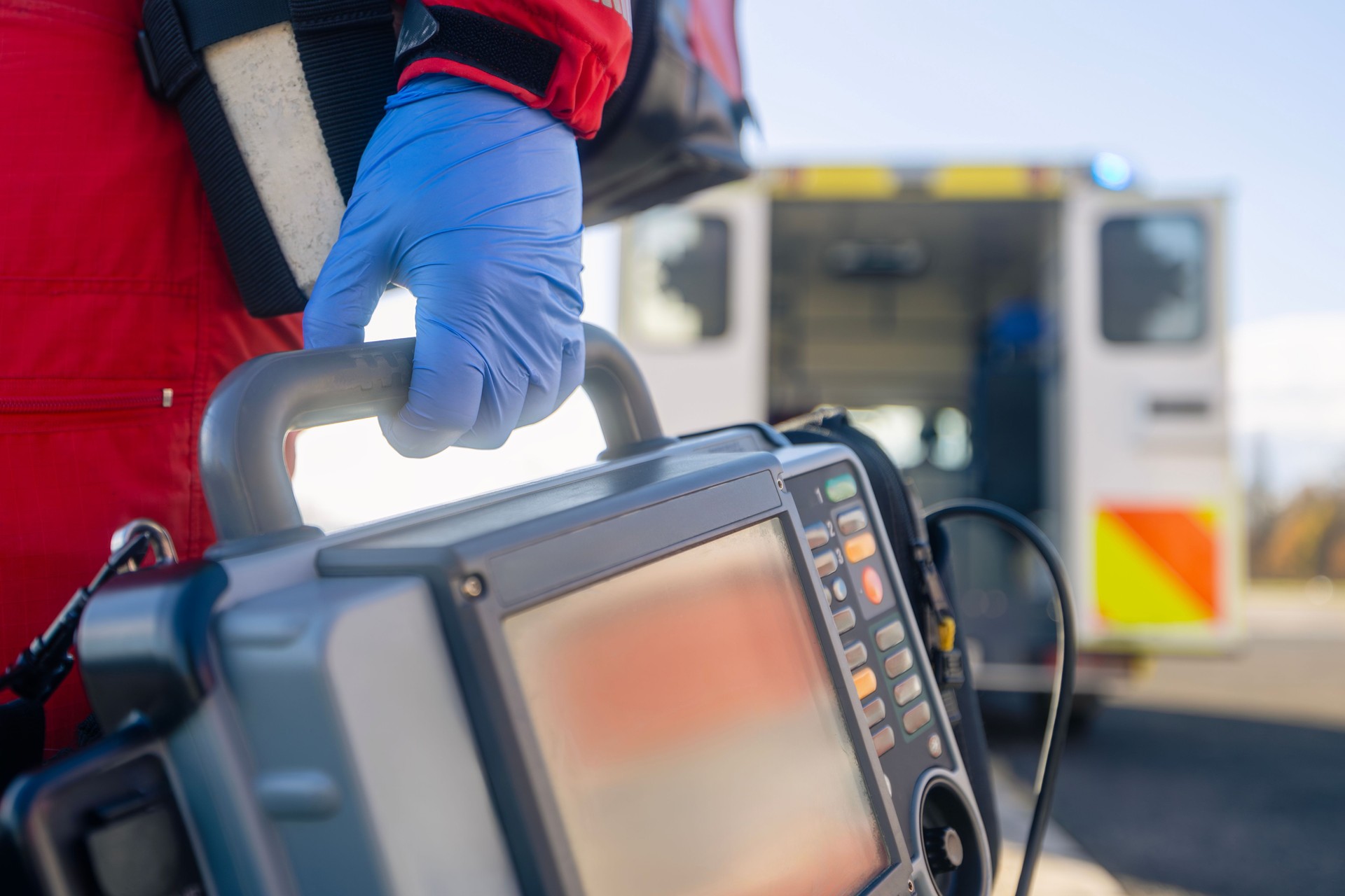 Paramedic hand in blue surgical gloves while running with defibrillator monitor against ambulance car